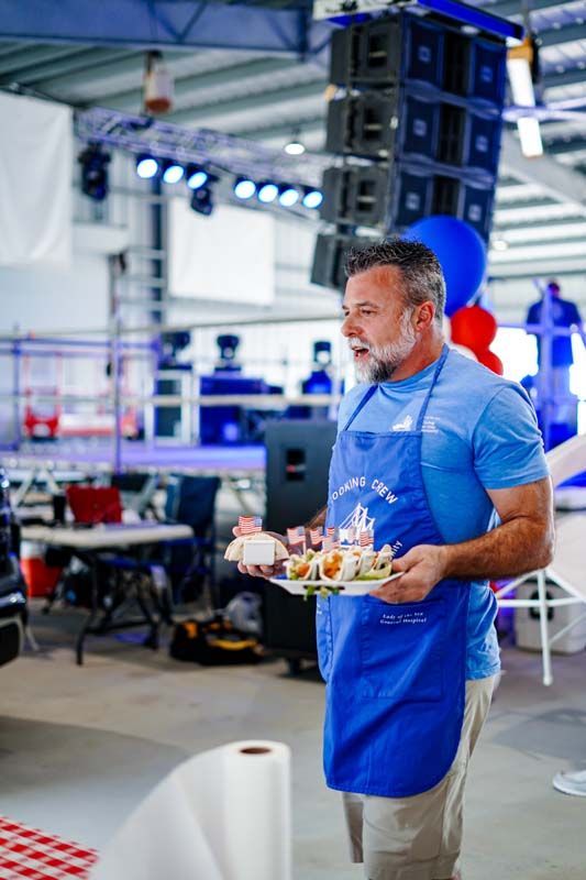 A man in a blue apron is holding a tray of food.