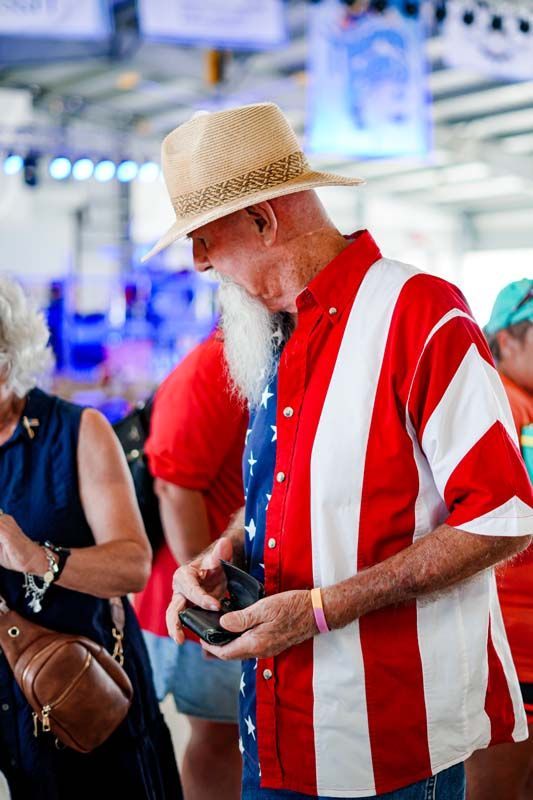 A man with a beard is wearing a red , white and blue shirt.