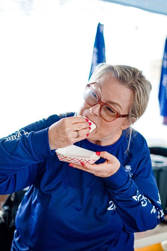 A woman in a blue shirt is eating from a styrofoam container.