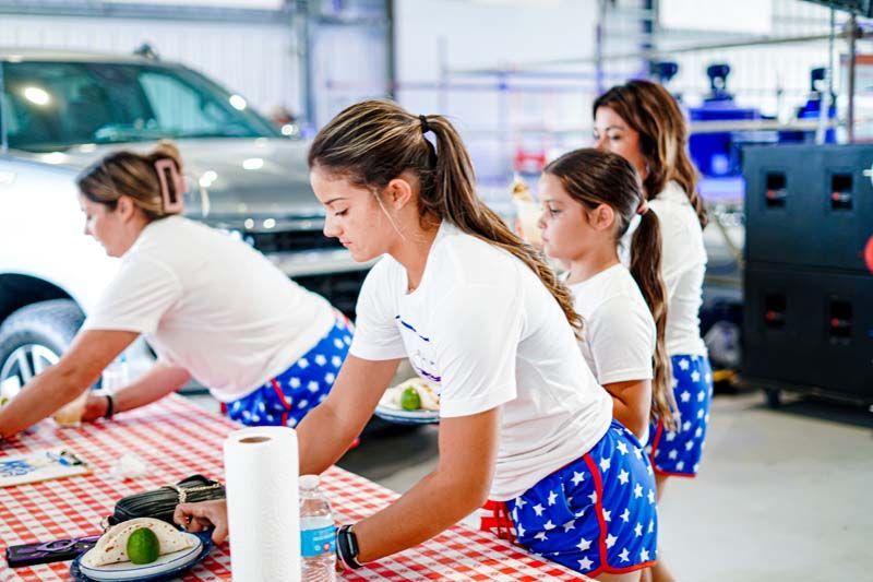 A group of women are standing around a table preparing food.