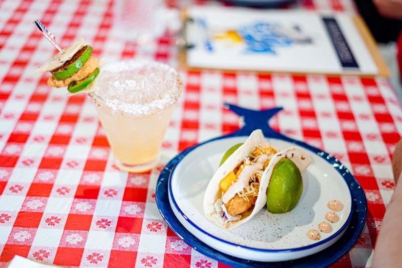 A plate of food and a drink on a checkered table cloth.