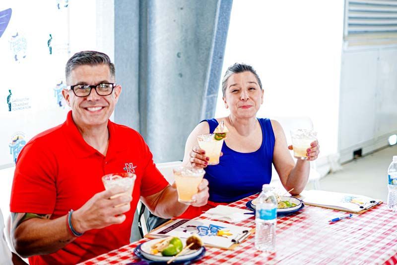 A man and a woman are sitting at a table holding drinks.