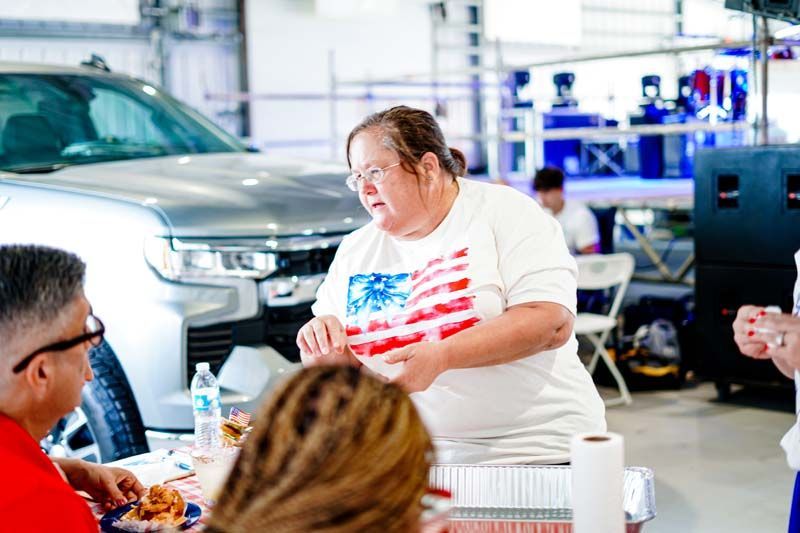 A group of people are sitting at a table in front of a car.