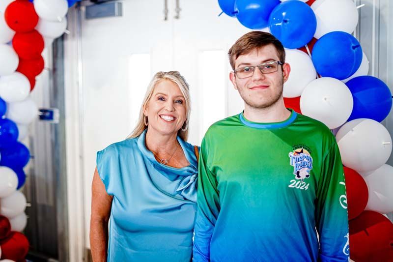 A woman and a boy are standing next to each other in front of balloons.
