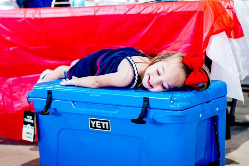 A little girl is laying on top of a blue yeti cooler.