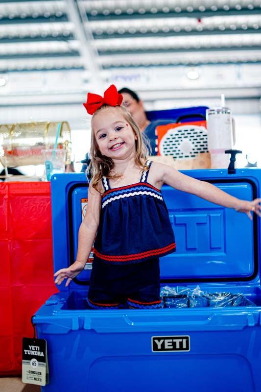A little girl is standing next to a blue yeti cooler.