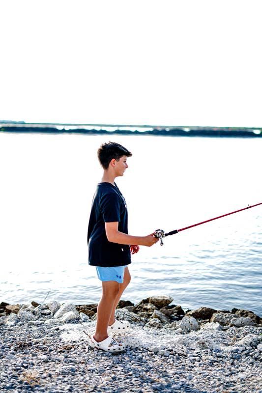 A young boy is fishing on the shore of a lake.