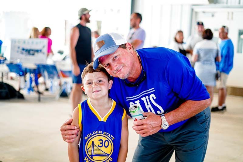 A man and a boy are posing for a picture . the boy is wearing a golden state warriors jersey.