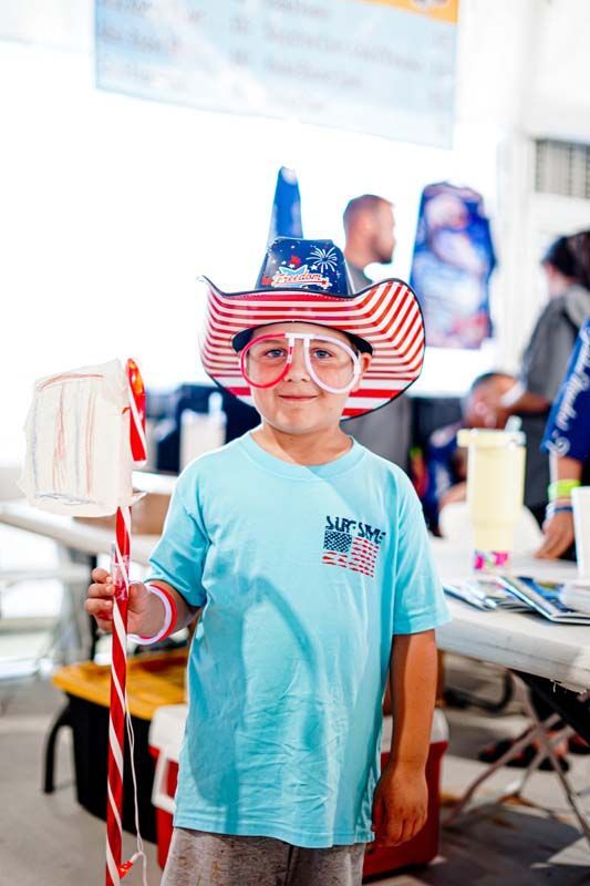 A young boy wearing a cowboy hat and glasses is holding a candy cane.