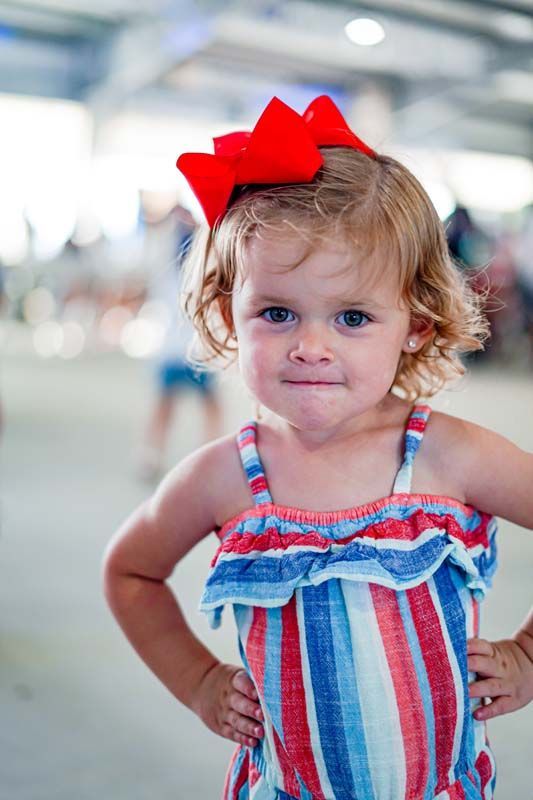 A little girl wearing a red bow in her hair is standing with her hands on her hips.