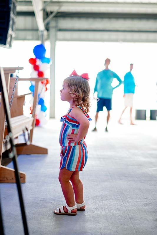 A little girl in a striped jumpsuit is standing on a concrete floor.