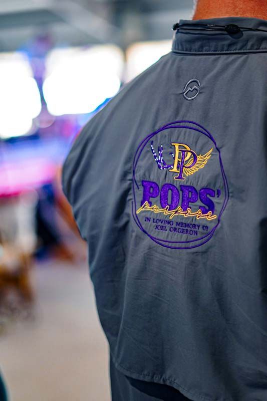 A man wearing a gray jacket with a purple logo on the back.