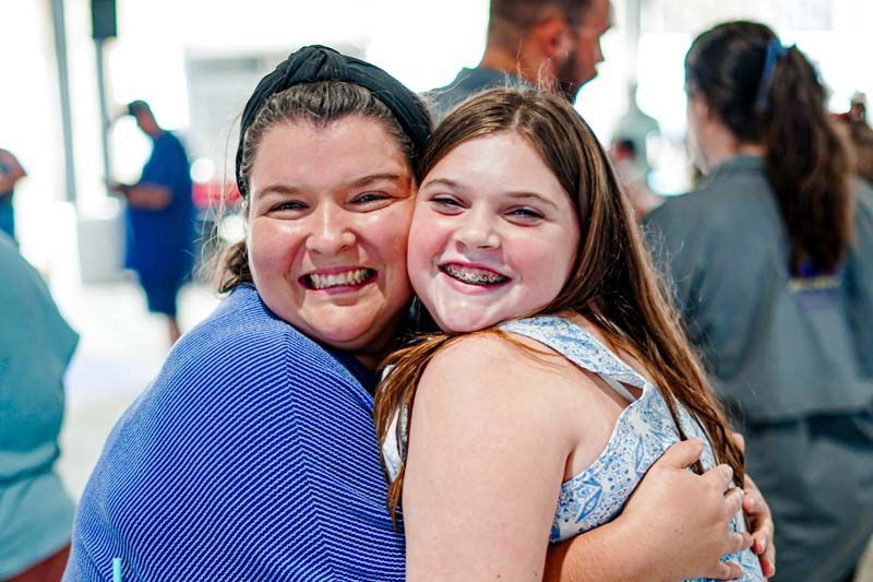 A woman and a young girl are hugging each other and smiling for the camera.