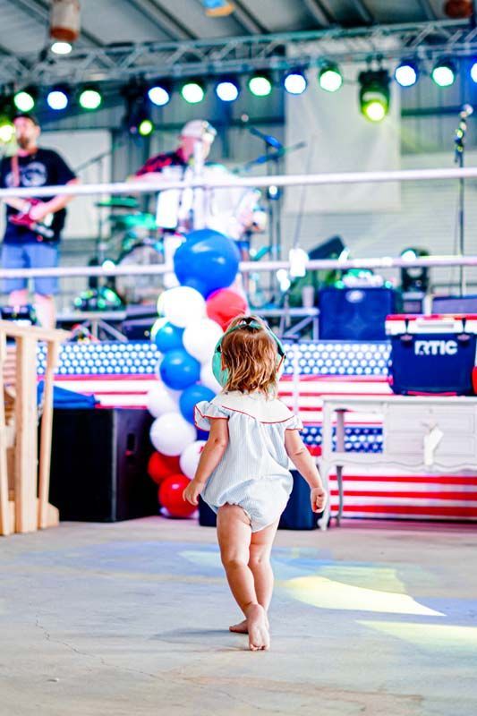 A little girl is walking towards a stage with balloons in the background.