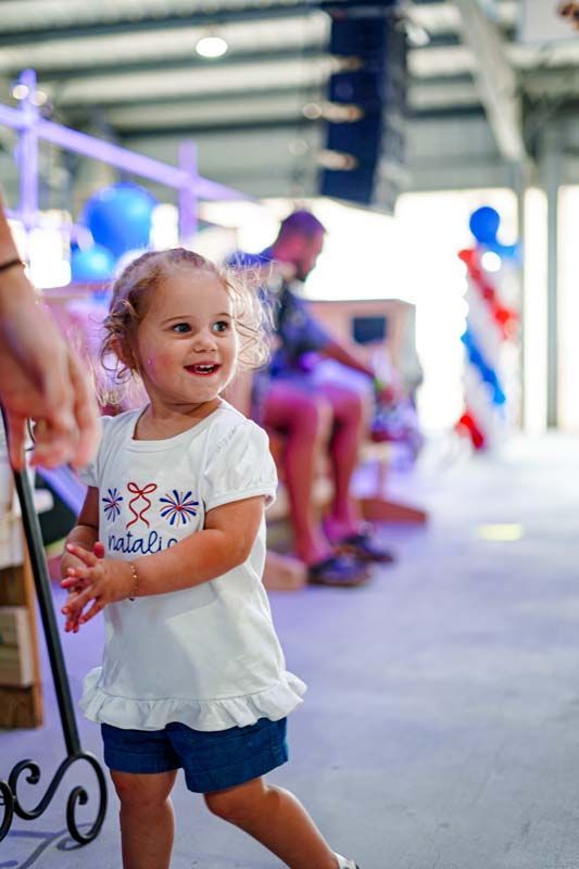 A little girl in a white shirt and blue shorts is standing in a room.