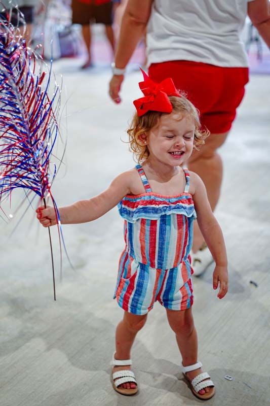 A little girl in a red , white and blue striped jumpsuit is holding a balloon.