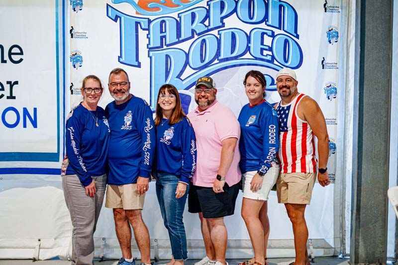 A group of people are posing for a picture in front of a tarpon rodeo sign.