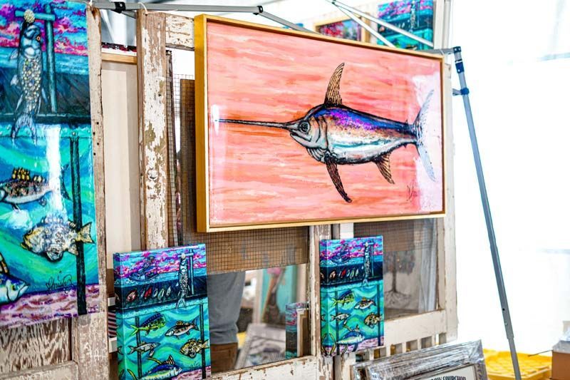 A painting of a marlin is hanging on a wooden easel.