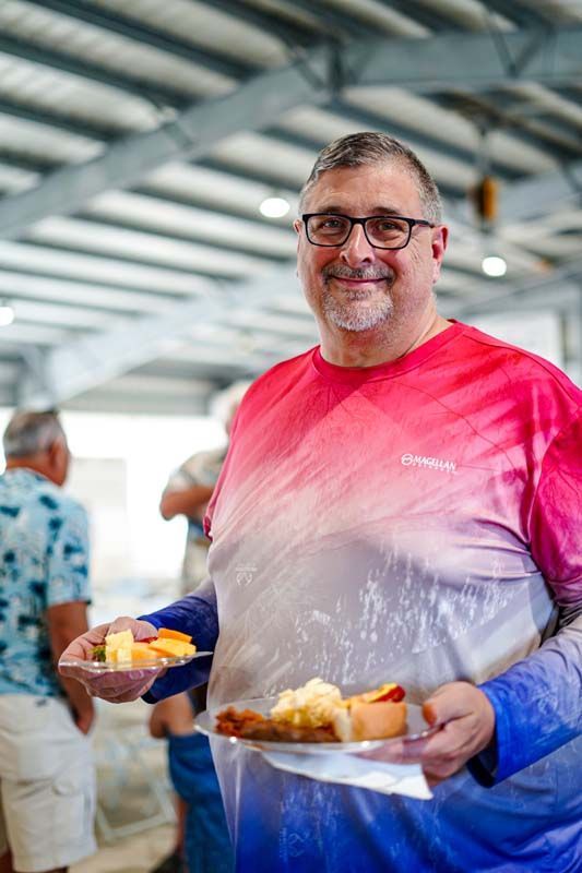 A man in a tie dye shirt is holding a plate of food.