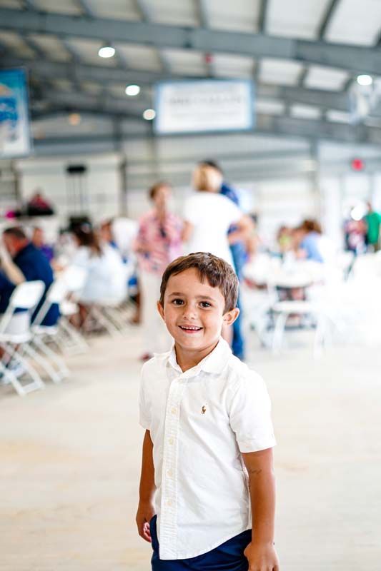 A young boy in a white shirt is standing in front of a crowd of people.