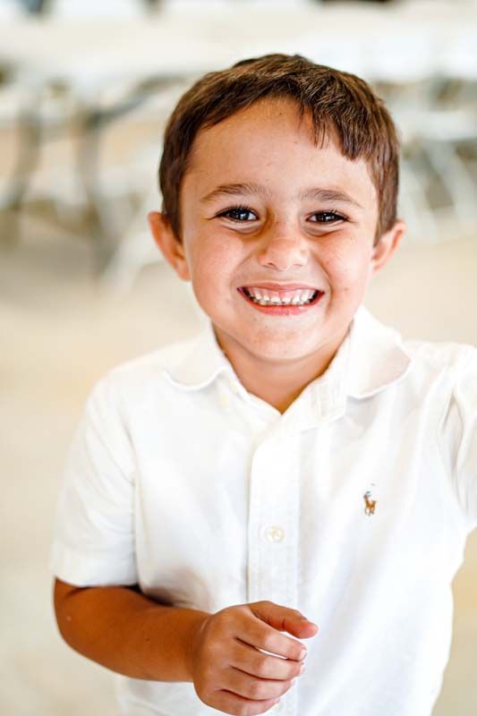 A young boy in a white polo shirt is smiling for the camera.