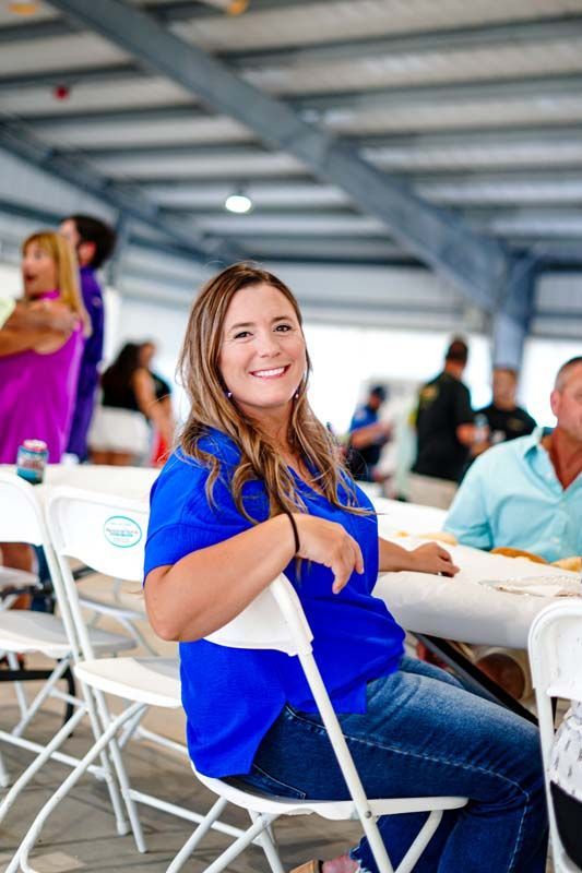 A woman in a blue shirt is sitting in a white folding chair at a table.