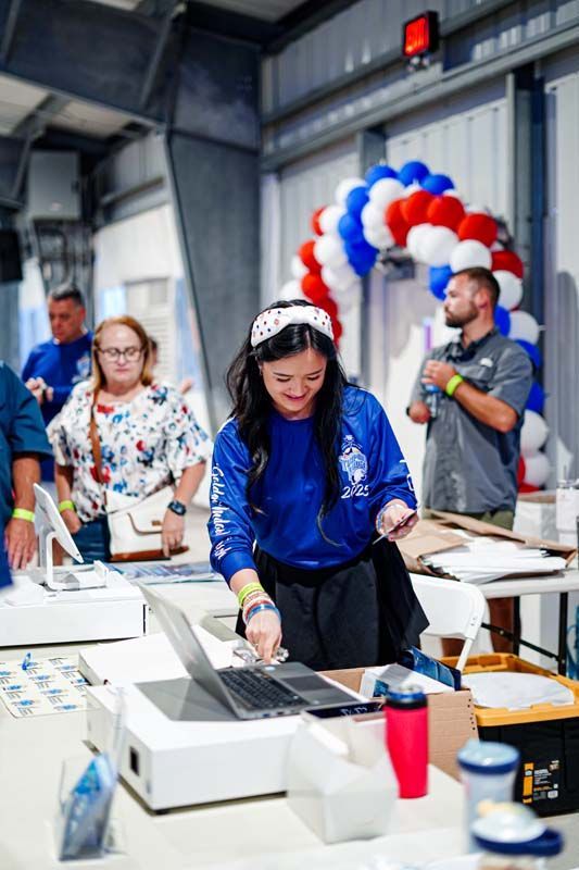 A woman is using a laptop computer at a table with balloons in the background.