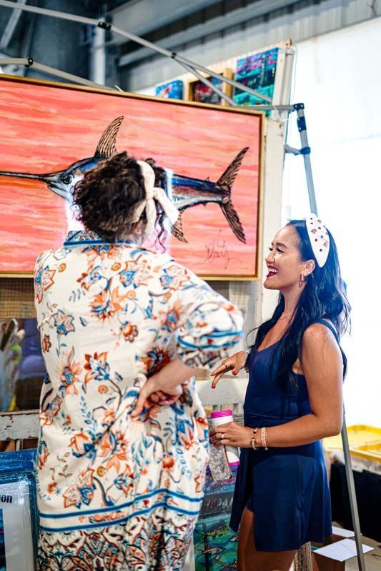 Two women are standing next to each other in front of a painting of a fish.