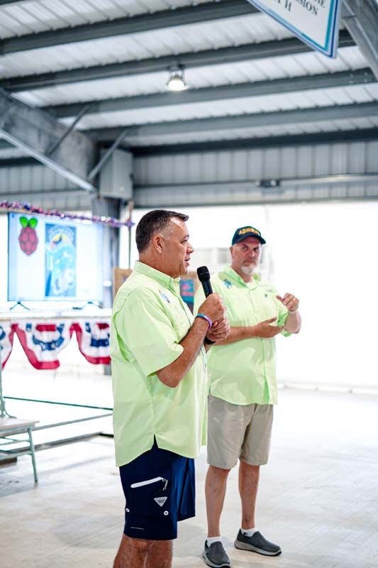 Two men are standing next to each other talking into microphones.