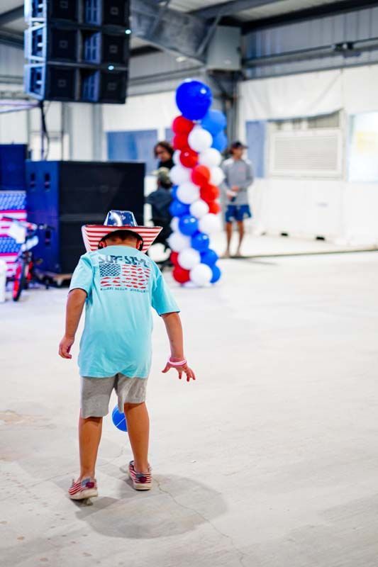 A little boy wearing a cowboy hat is walking in a room with balloons.