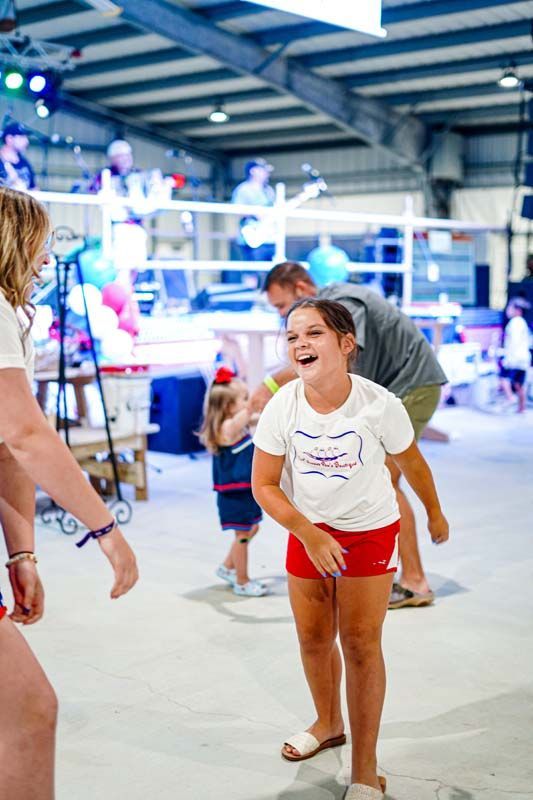 A little girl is laughing while standing in a room with people.