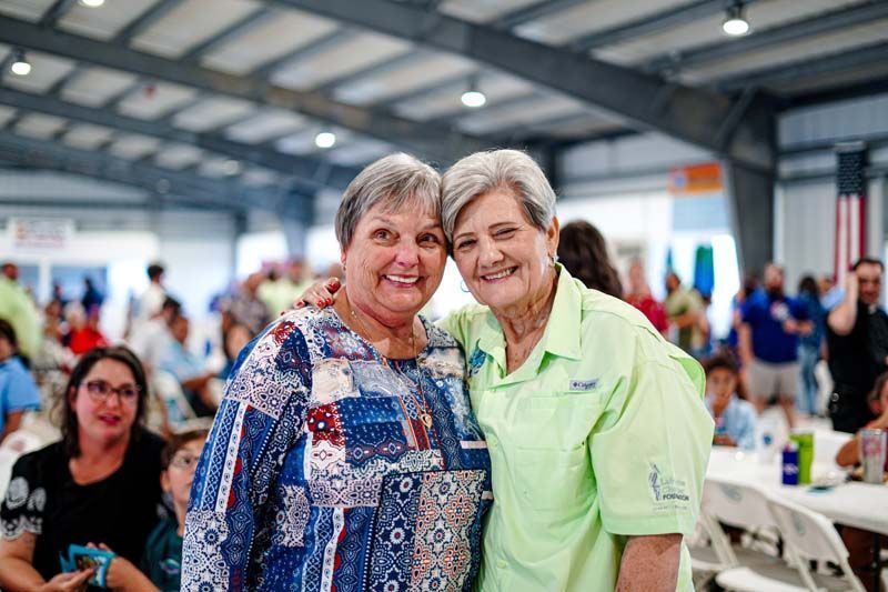 Two older women are posing for a picture together at a picnic.