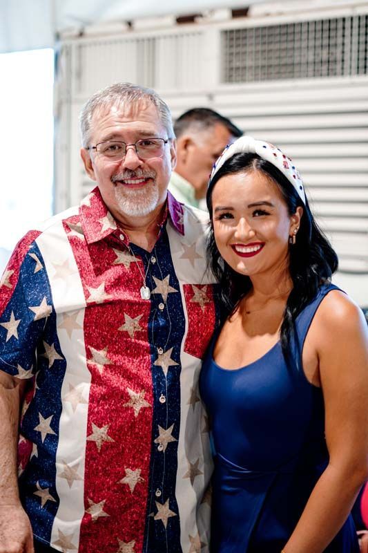 A man in an american flag shirt is posing for a picture with a woman in a blue dress.