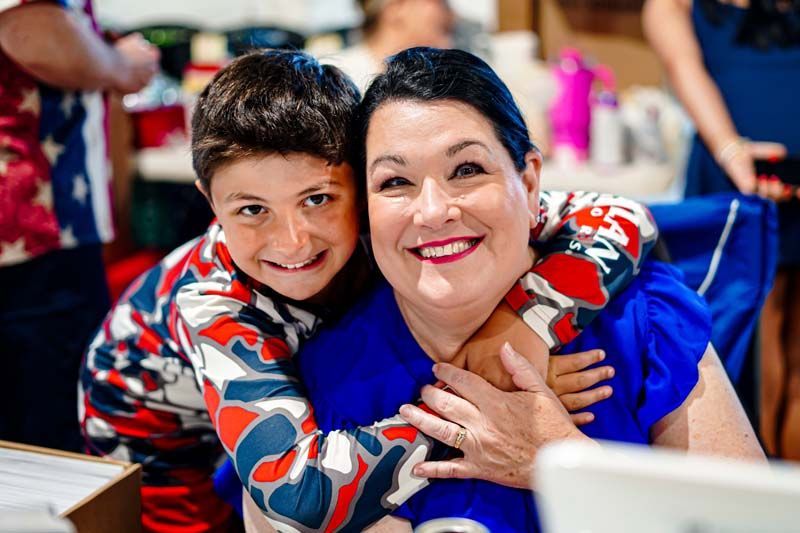 A woman and a boy are hugging each other and smiling for the camera.