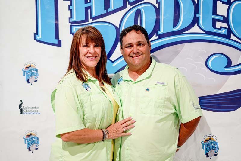 A man and a woman are posing for a picture in front of a sign that says rodeo.