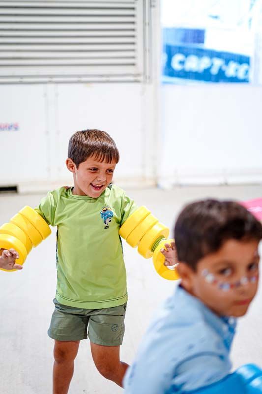 A boy in a green shirt is wearing yellow arm floats.