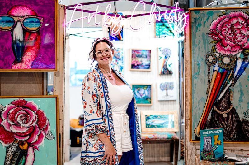A woman is standing in front of a wall of paintings.