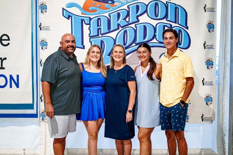 A group of people are posing for a picture in front of a tarpon rodeo sign.