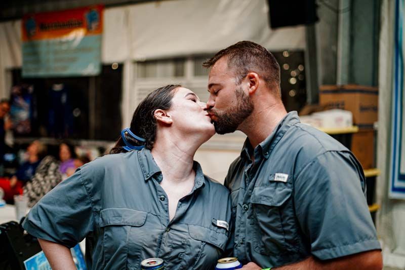 A man and a woman are kissing while holding cans of beer.