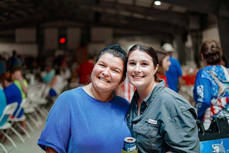 Two women are posing for a picture together in a crowded room.