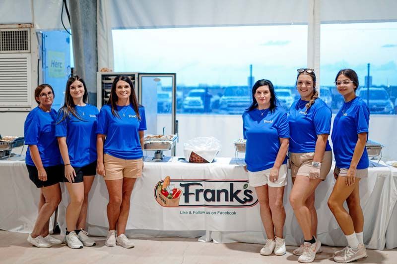A group of women in blue shirts are standing in front of a table.