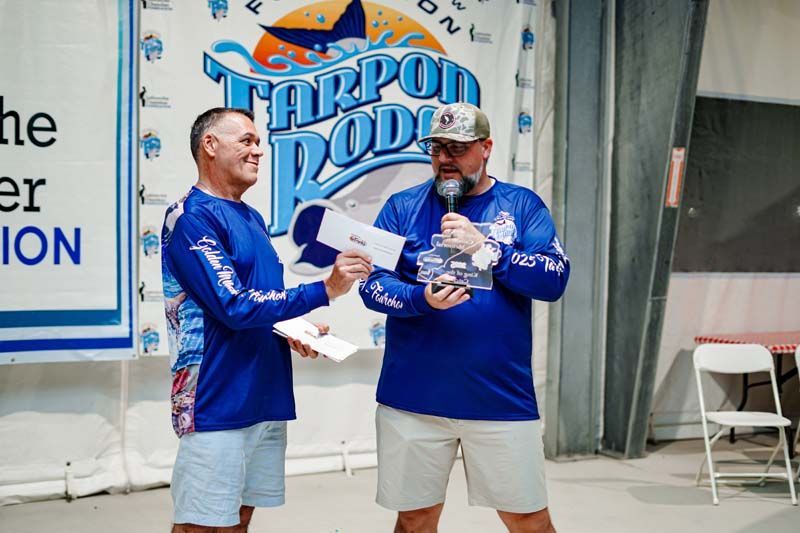 Two men are standing next to each other in front of a tarpon rod sign.