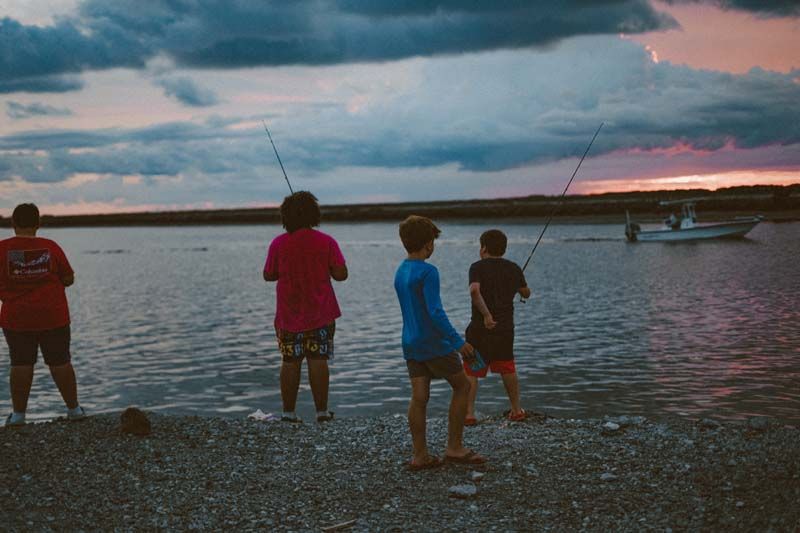 A group of people are fishing in the water at sunset.