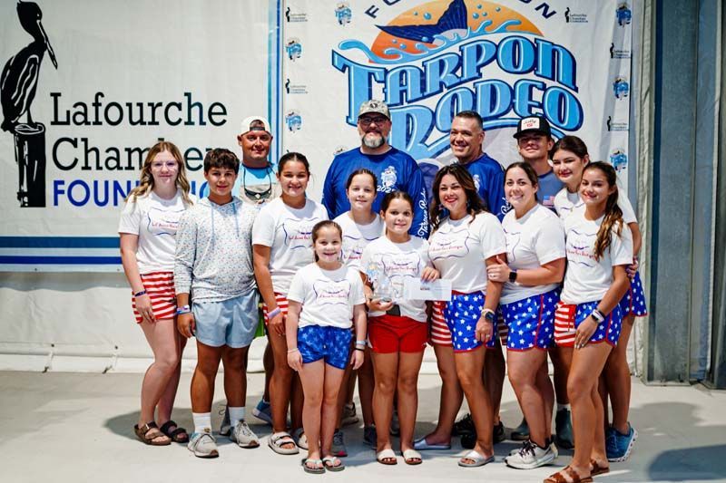 A group of people are posing for a picture in front of a tarpon rodeo sign.