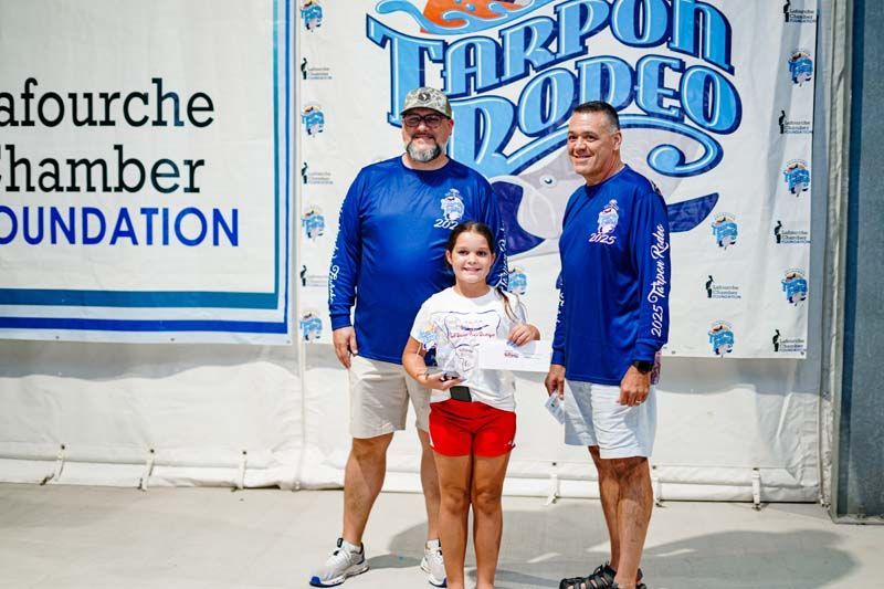 Three men and a little girl are standing in front of a tarpon rodeo sign.
