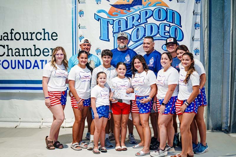 A group of people are posing for a picture in front of a tarpon rodeo banner.