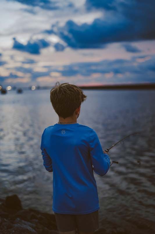 A young boy is fishing in the water with a fishing rod.