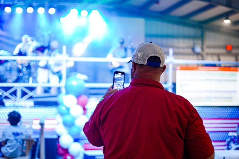 A man in a red shirt is taking a picture of a band on stage.