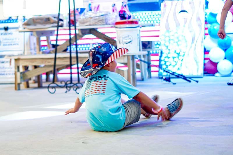 A little boy is sitting on the ground wearing a patriotic hat.