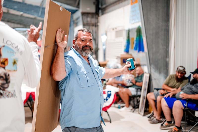 A man is holding a piece of cardboard and a can of beer.